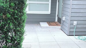 Een huis met grijze bekleding, een raam, een deur en een kleine tuin met een haag.