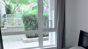 Een slaapkamer met een groot raam, een bed en uitzicht op een tuin en straat.