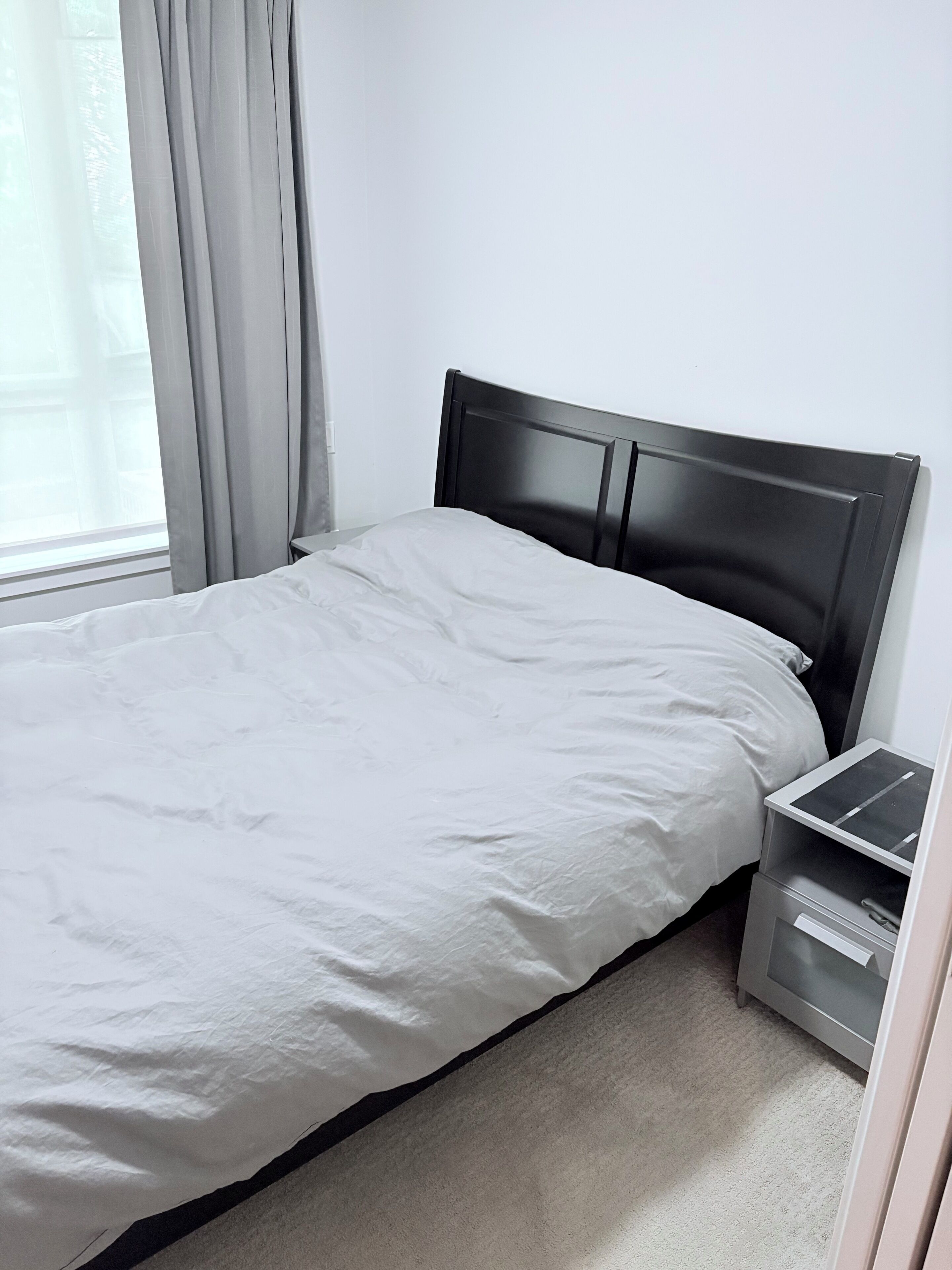 Una cama individual con sábana blanca, cabecera oscura y mesita de noche con cajón.