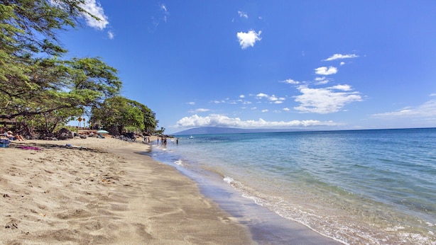 A beach with clear water, a sandy shore, and a mountain in the distance. - Lux Ocean View Penthouse 2 Kings+, Steps to Beach (Lahaina)