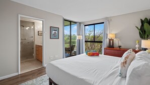 A bedroom with a large bed, a wooden dresser, a nightstand, a lamp, and a view of the outdoors. - Lux Ocean View Penthouse 2 Kings+, Steps to Beach (Lahaina)