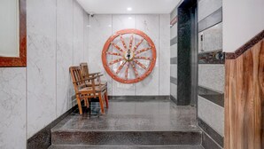 A marble wall with a large decorative wheel, a wooden chair, and a staircase. - Premium Hotel Aditya Inn (Dharwad)