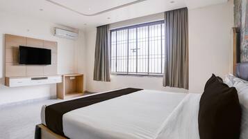 A hotel room with a bed, a TV mounted on the wall, a window with curtains, and a flat-screen TV.