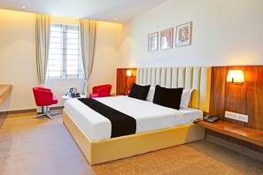 A hotel room with a large bed, two red chairs, a bedside table with a lamp, and a window with curtains. - Premium Stays by Hotel Trubell Electronic City (Anekal)