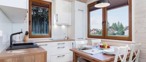 A modern kitchen with wooden cabinets, a dining table set for four, and large windows offering a view of the surrounding area.