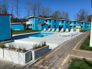 A pool area with lounge chairs and a building with blue siding. - Comfortable Holiday Home , Summer Pool (Rewal)