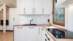 A modern kitchen with white cabinetry, a black faucet, and a window with a view of trees. - Comfortable Holiday Home , Summer Pool (Rewal)