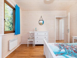 A room with wooden walls, a bed with a colorful bedspread, a white dresser, a chair, and a window with blue curtains. - Comfortable Holiday Home , Summer Pool (Rewal)