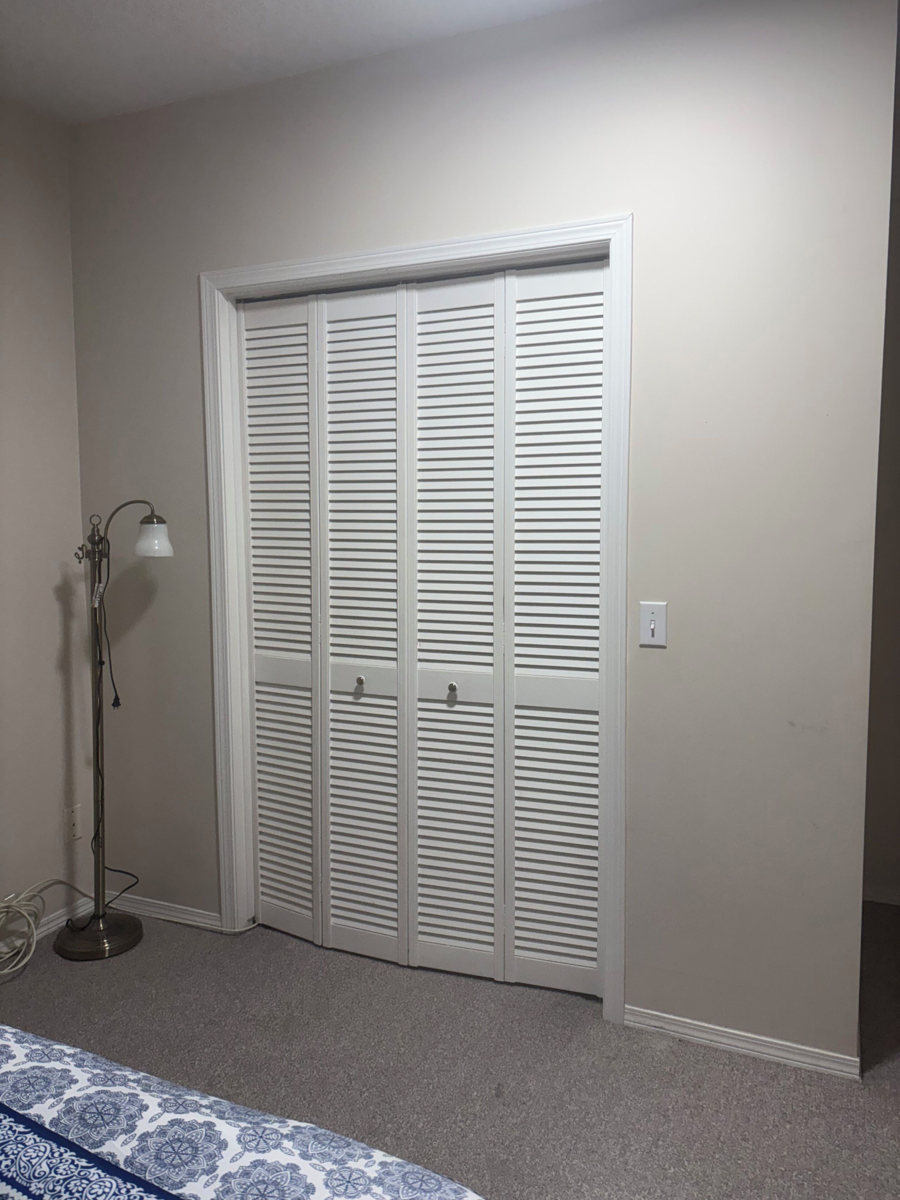 A room with a white closet, a lamp, and a patterned bedspread.. •	Family-Friendly Oasis: Spacious Suite  with convenient  Amenities near airport
