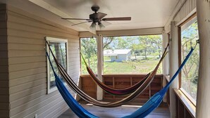Una hamaca en una habitación con piso de madera, ventilador de techo y ventanas grandes.
