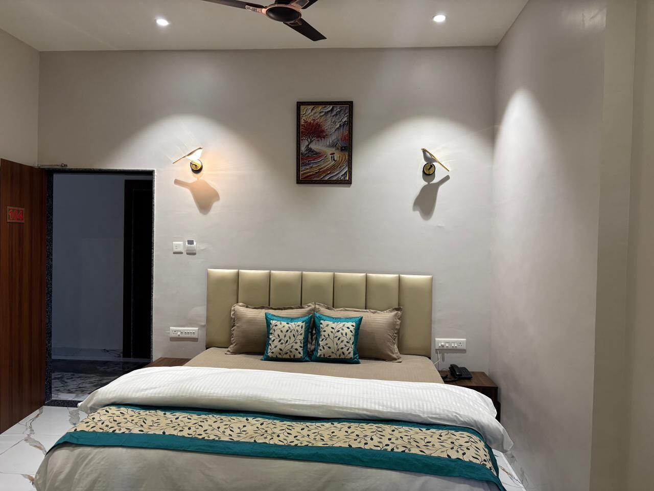 A bedroom with a bed, a headboard, bedside tables, a wall-mounted light, and a ceiling fan.