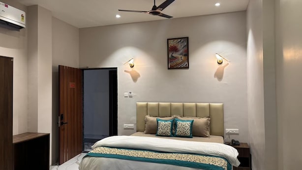 A bedroom with a bed, a ceiling fan, wall-mounted lights, and a door.
