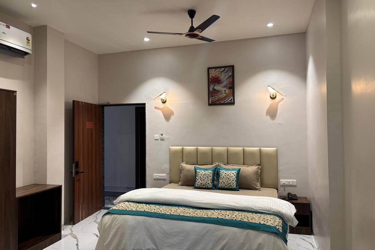 Quarto com cama, ventilador de teto, luminárias na parede e uma porta.