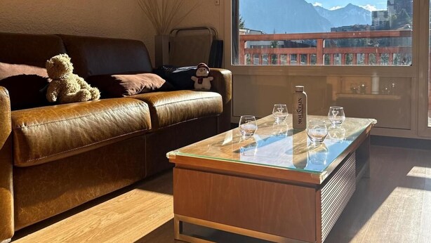 Ein Wohnzimmer mit Ledersofa, Couchtisch aus Glas und großem Fenster mit Blick auf die Berge.