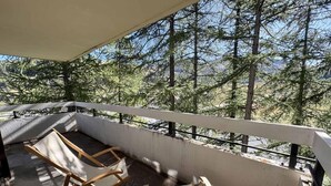 Ein Balkon mit zwei Holzliegen, einem Betonboden und Blick auf eine bewaldete Gegend.