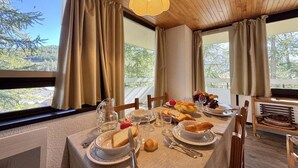Ein Esstisch ist gedeckt mit Tellern, Gläsern und Speisen, mit Blick auf Bäume durch große Fenster.