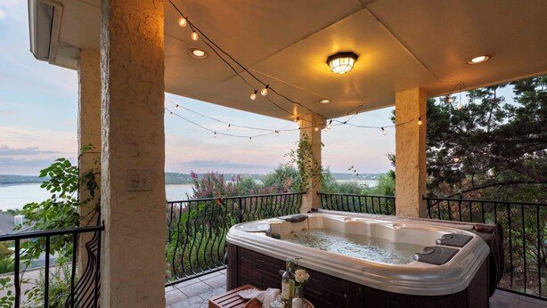 A hot tub on a balcony with a view of a body of water and greenery.