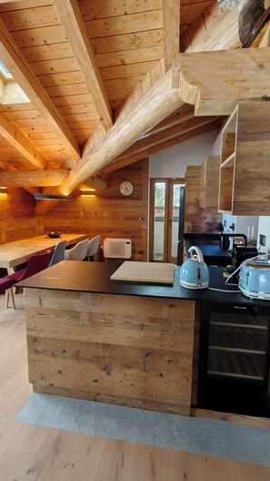 A wooden cabin interior with a dining area, kitchen, and a large wooden beam ceiling. - Villa Les Clochards Luxury ski-in/ski-out apartments, SPA, Matterhorn view, wifi (Breuil-Cervinia)
