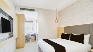 A modern hotel room with a large bed, a flat-screen TV mounted on the wall, a small seating area with a chair and table, and a patterned wallpaper on the walls. - Townhouse Oak Aecs Layout Brookfield (Bengaluru)