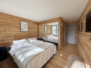 A bedroom with a wooden wall, a bed with white bedding, a mirror, and a door leading to another room. - 300m from shops, 5th floor, terrace, ski locker, 74m², Vars (Vars)