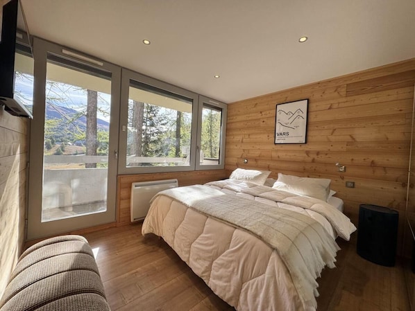 A bedroom with a bed, large windows, a radiator, and a wooden wall. - 300m from shops, 5th floor, terrace, ski locker, 74m², Vars (Vars)