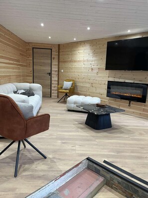 Ein modernes Wohnzimmer mit einer Couch, einem Sessel, einem Hocker und einem Kamin.