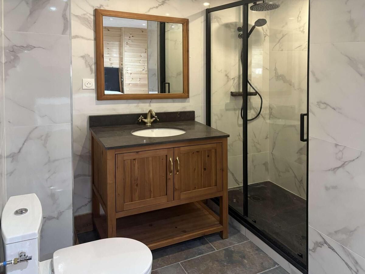 A bathroom with a wooden vanity, a white sink, a mirror, a glass shower enclosure, and a toilet.