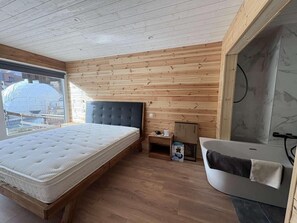 Ein Schlafzimmer mit Bett, Nachttisch und einem Badezimmer mit Badewanne, sowie Holzwänden.