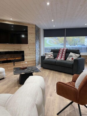 Ein modernes Wohnzimmer mit Kamin, Sofa, Couchtisch und Fernseher.