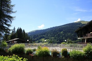 A mountain landscape with a wooden building and a white fence in the foreground. - Ski-in/ski-out & foot of the slopes, 1st floor, swimming pool, balcony, parking, 35m², Les Gets (Les Gets)