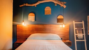 Una cama con cabecera de madera, dos lámparas colgantes y una escalera contra una pared azul.