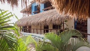Edificio de techo de paja con balcón de madera, rodeado de follaje tropical.