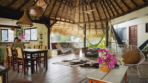 Una habitación con techo de paja, muebles de madera, un comedor y vistas a la vegetación.