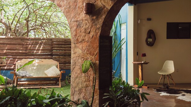 Una habitación con un arco de piedra, un banco de madera, plantas en macetas, un tapiz de cuero de vaca y una silla blanca.