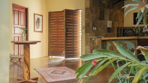 Una habitación con una puerta de madera, una mesa pequeña con un florero, un par de zapatos, una alfombra y una planta.