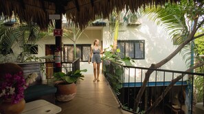 A woman walking in a covered outdoor area with a fire extinguisher, potted plants, and a thatched roof. - Punta Dreams (Brisas de Zicatela)