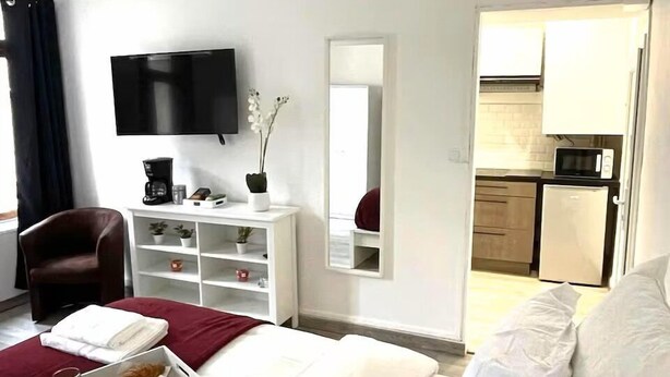 A hotel room with a bed, a TV, a desk with a coffee maker, a chair, and a kitchenette.