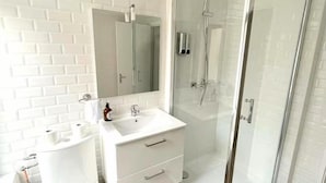 A bathroom with a white toilet, a sink, a mirror, and a glass-enclosed shower.