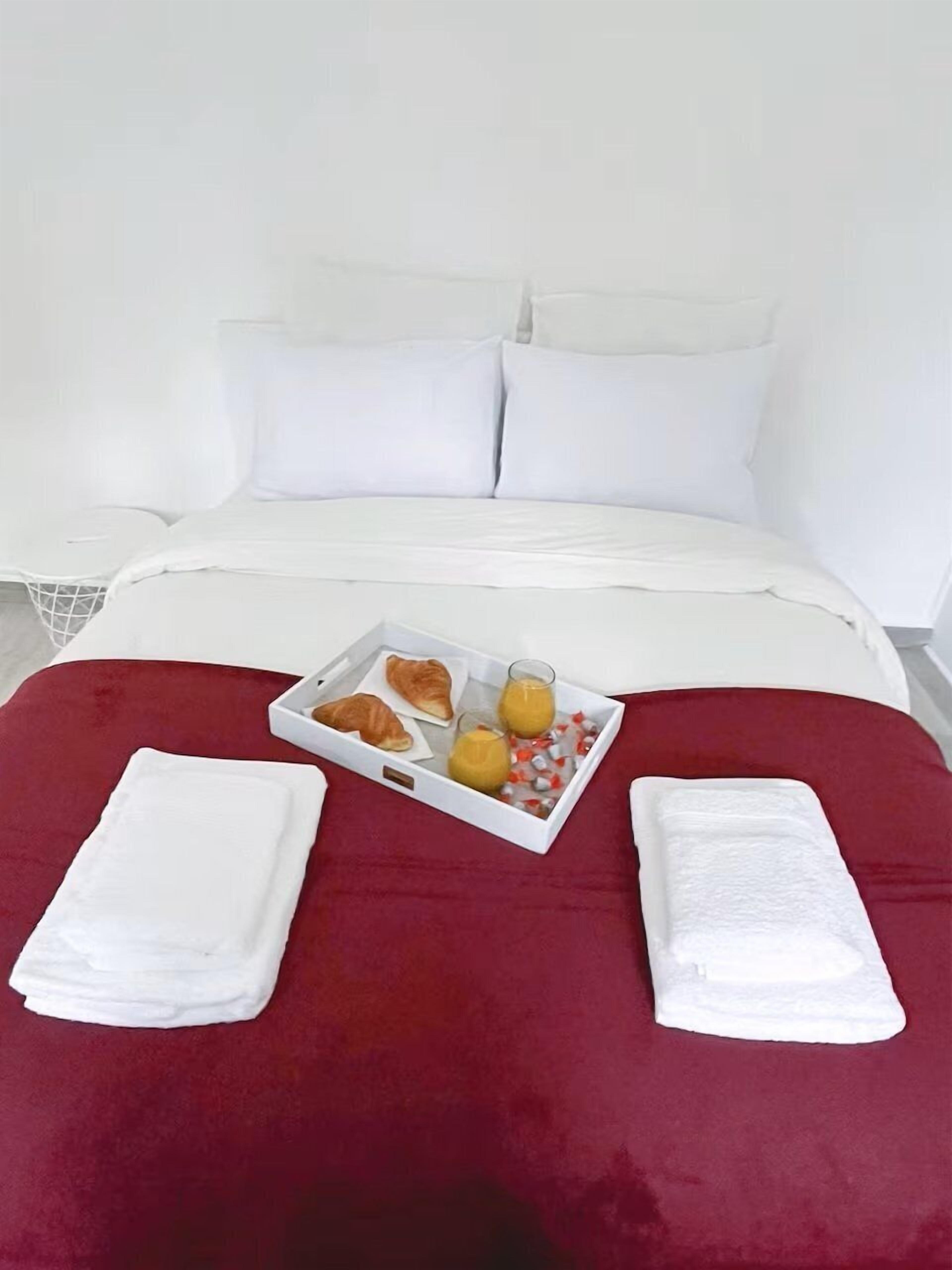 Un letto con copripiumino rosso, cuscini bianchi e un vassoio con croissant e succo d'arancia.