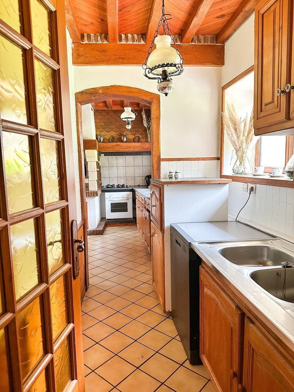 A kitchen with wooden cabinets, a tiled floor, and a hanging light fixture.