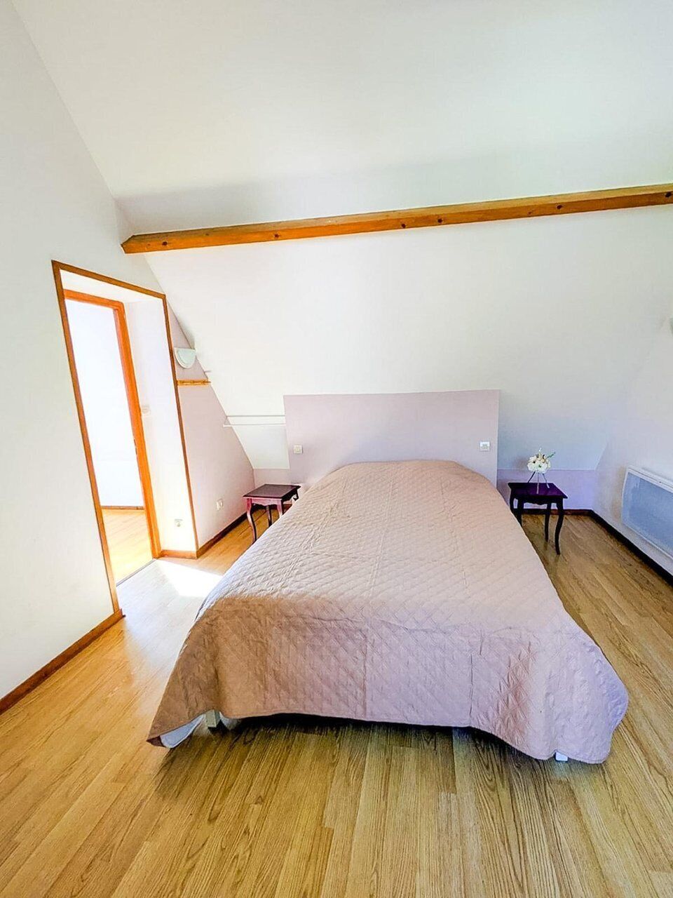 A bedroom with a sloped ceiling, a bed, a small table, and a chair.