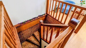 A wooden staircase with a handrail, a small table with a vase of flowers, and a window with a view of the sky.