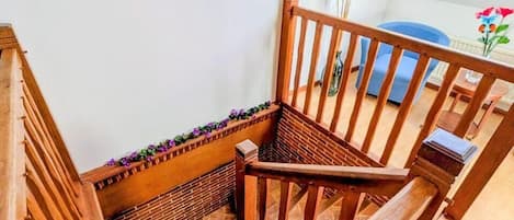 Una escalera de madera con barandilla, una mesita con un florero y un ventanal con vista al cielo.