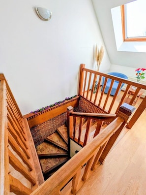 A wooden staircase with a handrail, a small table with a vase of flowers, and a window with a view of the sky.