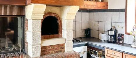 A kitchen with a brick oven, wooden beams, a clock, and a tiled backsplash.