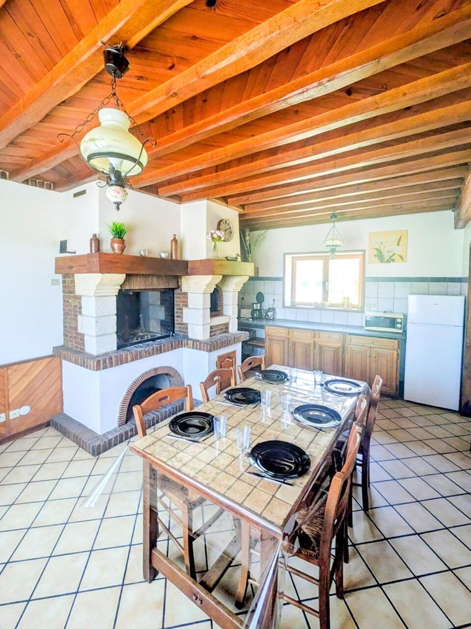 A rustic kitchen with a tiled floor, wooden ceiling beams, a central island with chairs, a built-in stove, and a window above the sink.
