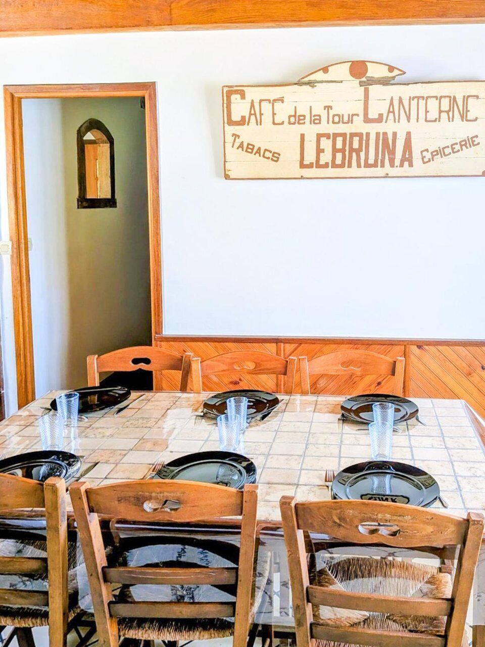 A dining area with a wooden table and chairs, a sign above the table, and a doorway leading to another room.