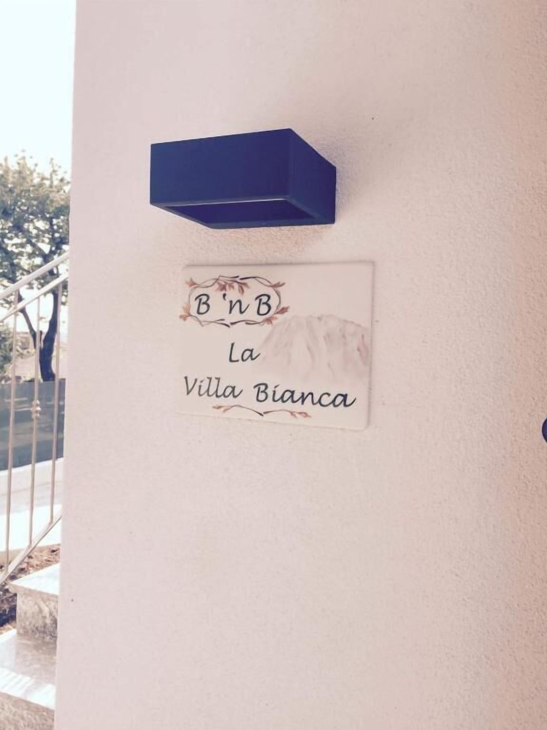 A sign with 'B'nB La Villa Bianca' on a wall, a blue shelf above it, and a staircase leading down.