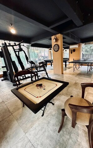 Uma academia com equipamentos de ginástica, mesa de pebolim e alvo de dardos.