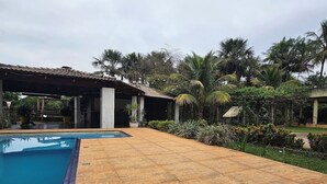 A swimming pool with a tiled deck, surrounded by palm trees and greenery.